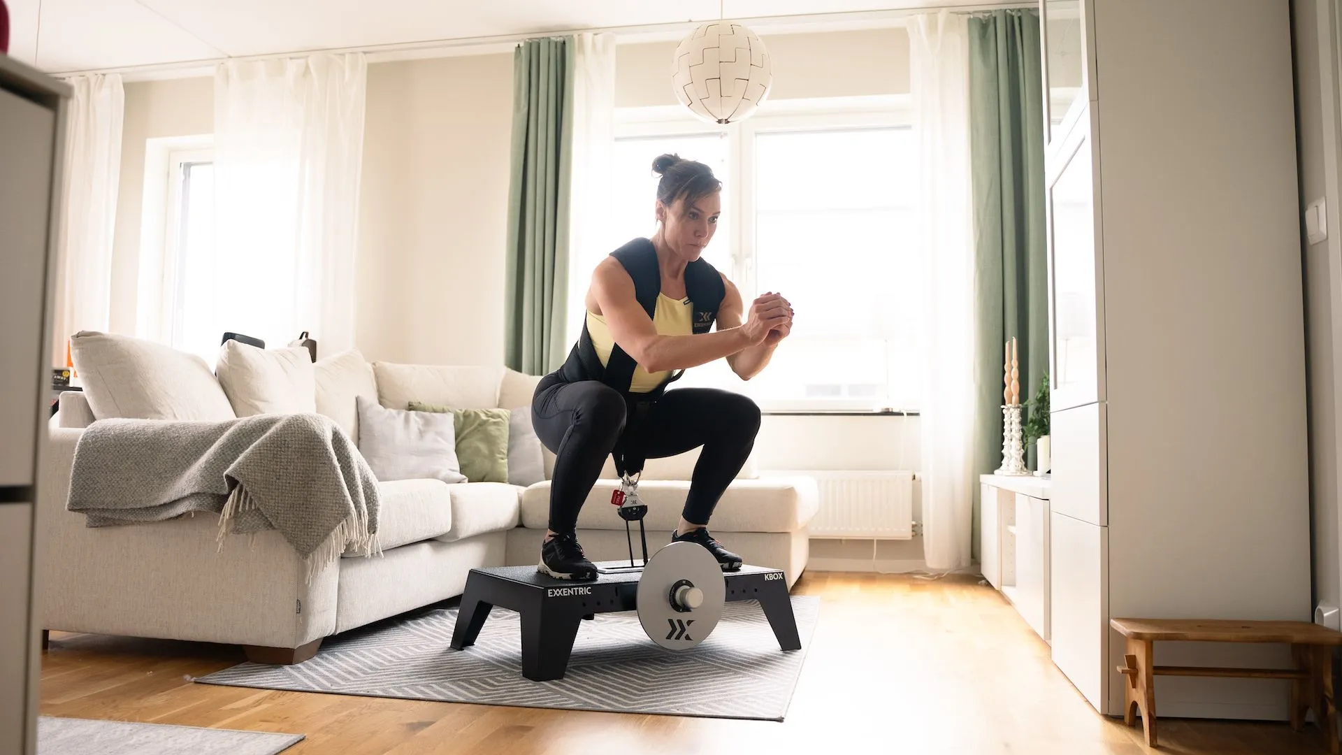 detail-2 sara_squatting_on_kbox_active_with_harness_and_m_flywheel_in_the_living_room.webp